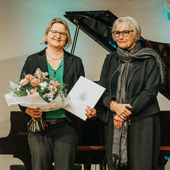 Prof. Dr. Andra Schromm und Prof. Gabriele Gillessen-Kaesbach stehen nebeneinander. Erstere hält eine Blumenstrauß und eine Urkunde.