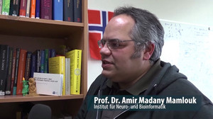 Amir Madany Mamlouk wird vor einer Bücherwand interviewt. Der Link öffnet das Video bei YouTube.